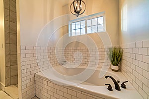 Built in oval bathtub with black faucet against white tiled wall of bathroom