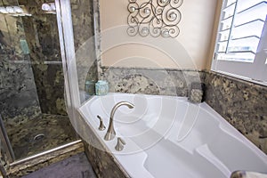 Built in white bathtub and shower stall inside a bathroom with marble wall