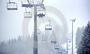 Bukovel, Ukraine - December 09, 2018: skiers carrying up near huge steel pillar, over tall fir trees on chairlift in fog