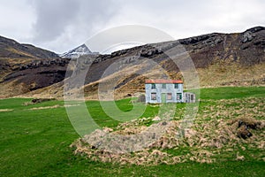 Bulandstindur mountain peak with snow on it. Blue abandoned farmhouse infront of it.