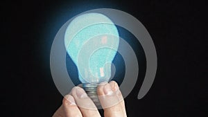 The bulb lights up in the hands of a young man, black background