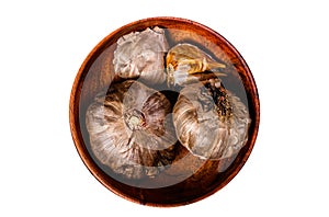Bulbs and cloves of fermented black garlic in a plate. Isolated, white background.