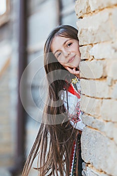 Bulgarian beautiful woman in ethnic folklore costume with bulgarian embroidery looking behind the wall bricks of old revival house