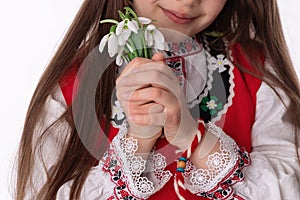 Bulgarian girl in ethnic folklore costume with bouquet of spring flowers snowdrops and martenitsa, Baba