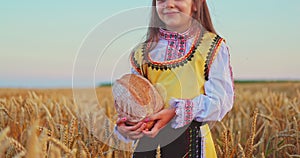 Bulgarian girl in ethnic folklore embroidery traditional costume with homemade bread in wheat Bulgaria