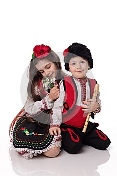 Bulgarian kids boy and girl in folklore clothes, spring snowdrops, flute, red white martenitsa March holiday Baba Marta, Bulgaria