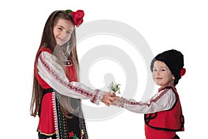 Bulgarian kids boy, girl in folklore costumes, spring flowers, martenitsa symbol of March Baba Marta holiday, Bulgaria