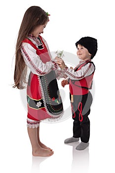 Bulgarian kids boy and girl in traditional ethnic folklore costumes with spring flowers, martenitsa symbol of March Baba Marta