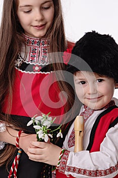 Bulgarian kids boy and girl in traditional folklore costumes with spring snowdrops, martenitsa symbol of Baba Marta