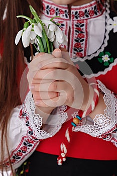 Bulgarian woman with bouquet spring snowdrop flowers and martenitsa March holiday Baba Marta, Bulgaria