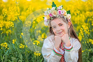 Bulgarian young girl with spring flower chaplet, ethnic folklore dress with bulgarian embroidery,yellow rapeseed field