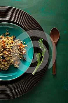 Bulgur pilaf with carrots and raisins on blue plate with wooden spoon and cillantro branch