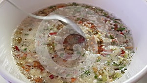 Bulgur porridge with vegetables is cooked in a white pan, a hand with a spoon will mix porridge during a boil.