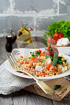 Bulgur with roasted peppers, tomatoes, parsley and feta cheese on a wooden background. Vegetarian dish. Selective focus
