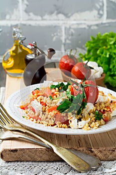 Bulgur with roasted peppers, tomatoes, parsley and feta cheese on a wooden background. Vegetarian dish. Selective focus