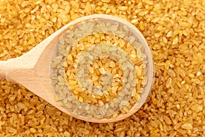Bulgur wheat background. Bulgur grains lie in a wooden spoon. View from above