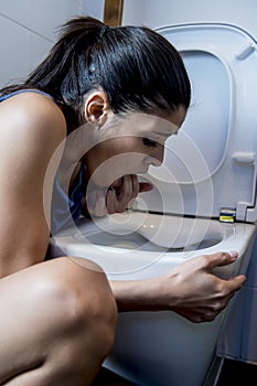 Bulimic woman feeling sick guilty fingers in mouth vomiting and throwing up in WC toilet