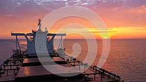 Bulk carrier loaded with grains underway under a crimson sky.