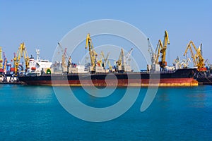 Bulk carrier ship in the port on loading. Bulk cargo ship under port crane bridge.