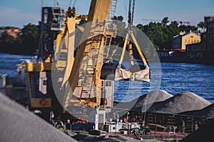 Bulk-handling crane unloading sand, road metal and gravel from cargo vessel ship, heavy vehicle and portal crane loader working