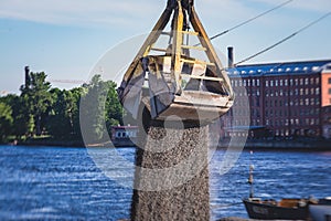 Bulk-handling crane unloading sand, road metal and gravel from cargo vessel ship, heavy vehicle and portal crane loader working