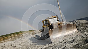 Bulldozer in background of open pit. Bulldozer stands motionless on background of natural phenomenon of rainbow in sky