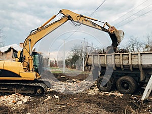 Bulldozer clearing land from old bricks and concrete from walls with dirt and trash. Backhoe machinery ruining house. Excavator