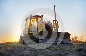 bulldozer on a construction site in the early morning against the blue sky and the rising sun