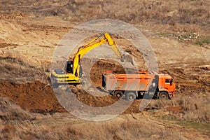 Bulldozer is gaining the earth in bucket and pours in truck