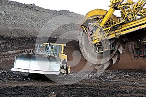 Bulldozer and huge mining excavator wheel in brown coal mine