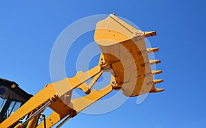 Bulldozer lifting bucket. Yellow excavator bucket against blue sky