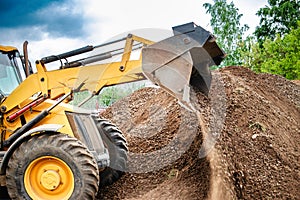 A bulldozer or a loader is actively digging dirt in a vast field, moving and reshaping the earth