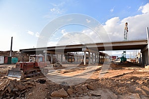 Bulldozer working at construction highway ramps and bridgeworks. Roundabout and traffic bridge construction. Road work on traffic