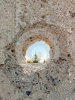 Bullet hole in a concrete wall close-up as a result of the fighting. Tree in the background in the hole