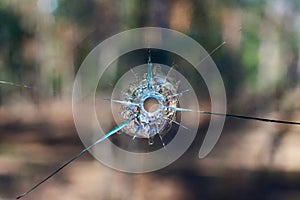 Bullet hole in glass close up on blurred nature background