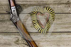 Bullets in the shape of heart next to rifle on rustic wooden background