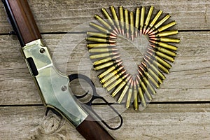 Bullets in the shape of heart next to rifle on rustic wooden background