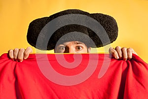 Bullfighter afraid with big hat hidden behind cape photo