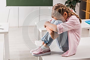 Bullied schoolkid covering face while sitting