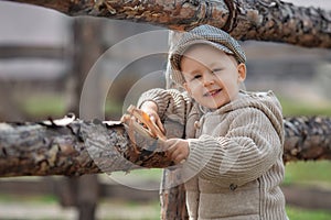 Bully boy kid with a slingshot aims at someone near a fence in the village outdoors. Rustic barefoot child boy with a