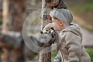 Bully boy kid with a slingshot aims at someone near a fence in the village outdoors. Rustic barefoot child boy with a