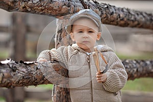 Bully boy kid with a slingshot aims at someone near a fence in the village outdoors. Rustic barefoot child boy with a