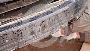 Bumper and radiator support of broken blue car. Registration plate is away. Man`s hands in white gloves take off some