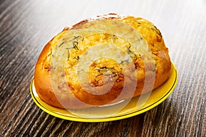 Bun with cheese and garlic in yellow saucer on wooden table