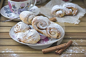 Bun-fight with freshly baked rolls of curd pastry, sprinkled with powdered sugar and a mug of hot tea on a wooden surface