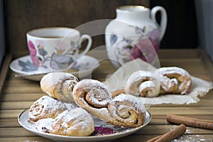 Bun-fight with freshly baked rolls of curd pastry, sprinkled with powdered sugar and a mug of hot tea on a wooden surface