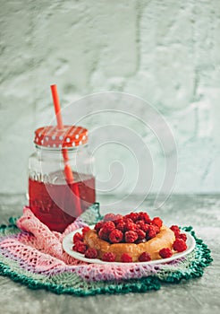 Bun with fresh raspberries on a white plate and red stewed fruit in a glass jar; summer light breakfast for a good mood