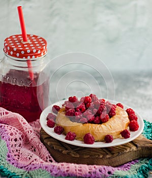 Bun with fresh raspberries on a white plate and red stewed fruit in a glass jar; summer light breakfast for a good mood