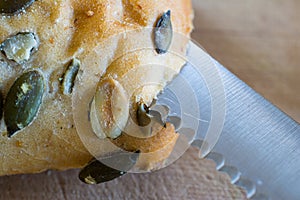 Bun with pumpkin seeds being cut with knife closeup.