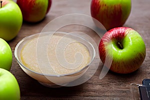 Bunch of apples put on a wooden table around a bowl of apple sauce